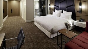 Une chambre d’hôtel avec un grand lit, un bureau, une chaise, une petite table avec un vase et un canapé rouge.