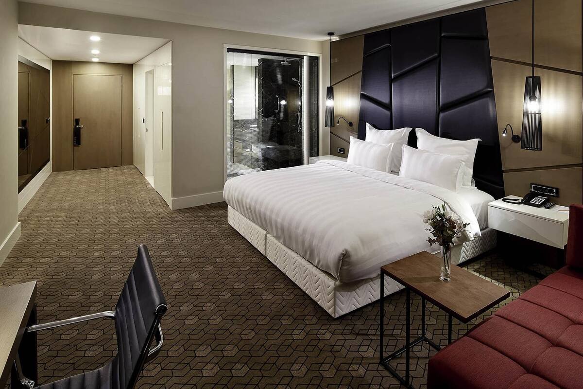 Een hotelkamer met een groot bed, een bureau, een stoel, een klein tafeltje met een vaas, en een rode bank.