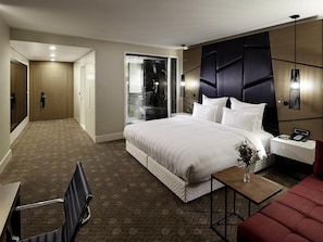 Une chambre d’hôtel avec un grand lit, un bureau, une chaise, une petite table avec un vase et un canapé rouge.