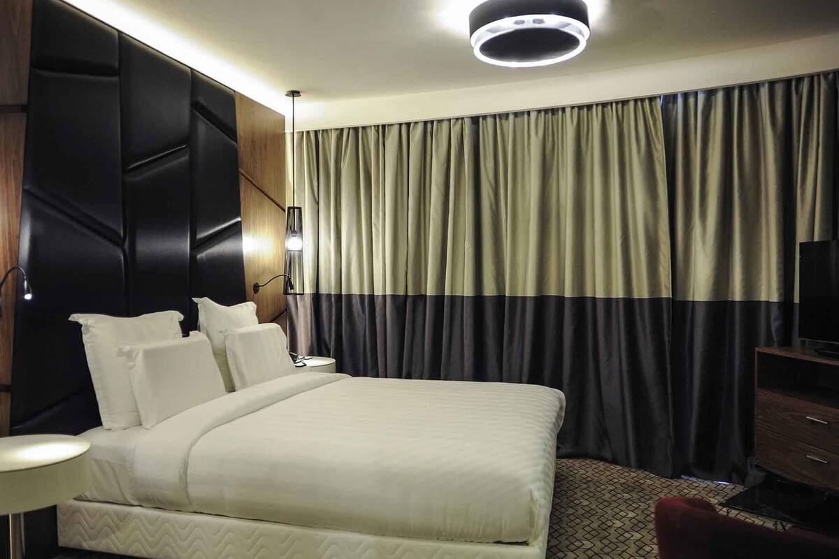 Een hotelkamer met een groot bed, een bureau, een stoel, een lamp en een gordijn.