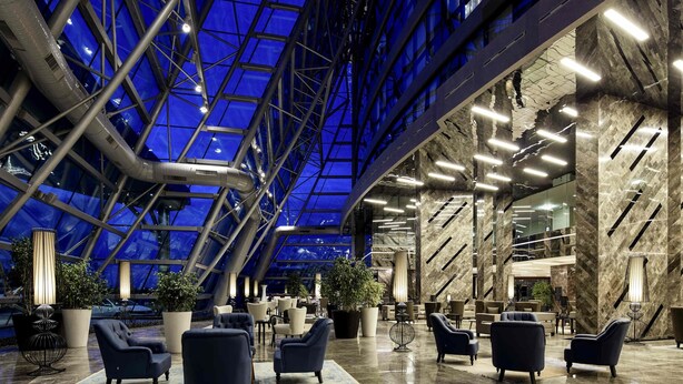 Een ruime lobby met een hoge plafond, grote ramen en moderne zithoeken.