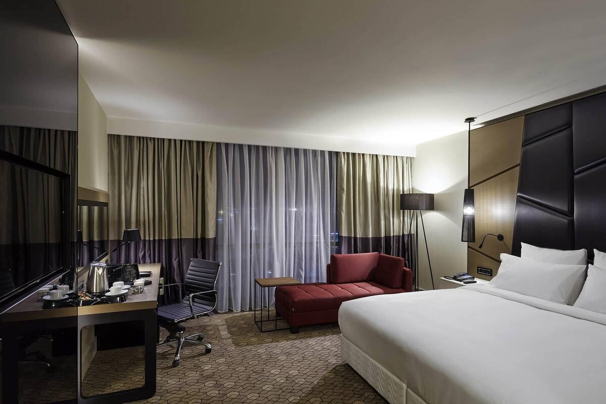 Een hotelkamer met een bed, bureau, stoel en een rode bank.
