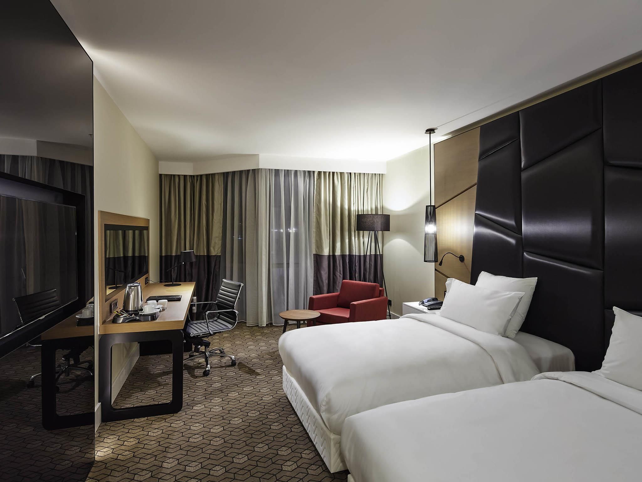 A hotel room with a bed, a desk with a chair, a TV, and a lamp.