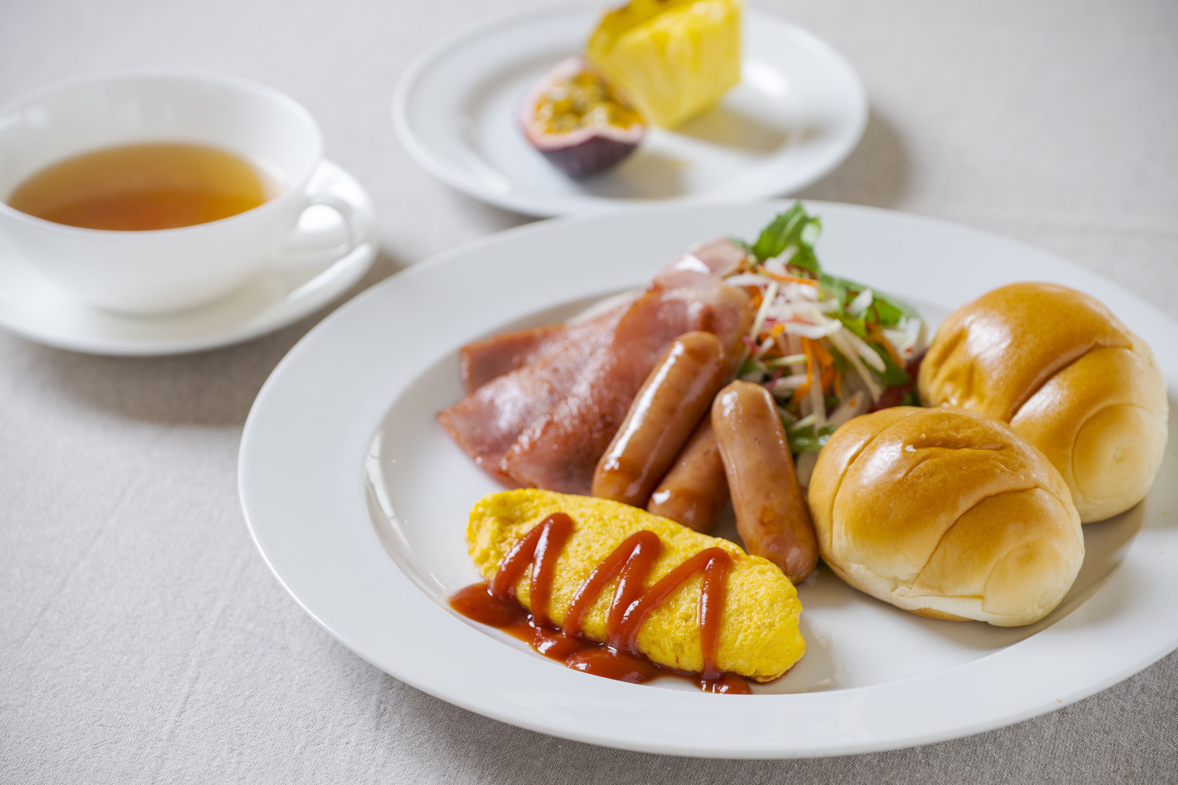 Une assiette avec une omelette roulée, des saucisses et des petits pains, et une tasse de thé.