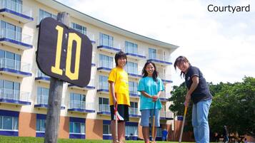 A courtyard with a sign marked '10', a group of people playing croquet, and a building with balconies in the background.