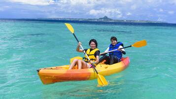 Two people kayaking on clear turquoise water with a distant island and a mountain in the background.