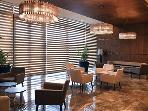 A modern lobby with tiered wooden slats, a large potted plant, leather sofas, and a marble floor.