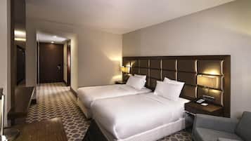 A hotel room with two beds, a desk, a chair, and a TV.