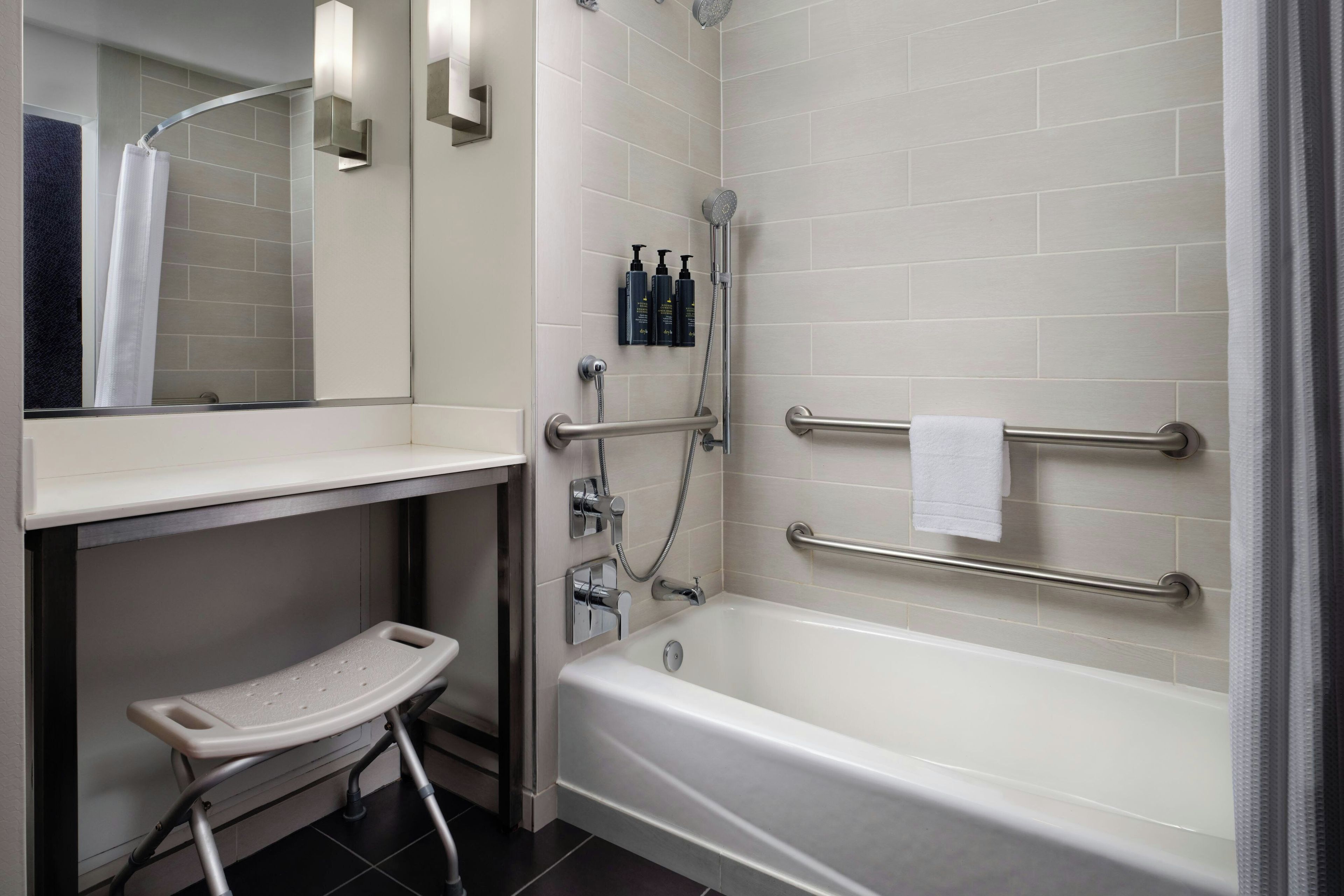 A modern bathroom with a bathtub, a shower, a handrail, and a step stool.