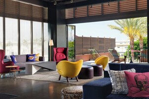 Una sala de estar moderna con un sofá, sillones y otomanas, ventanas amplias y vistas a palmeras.