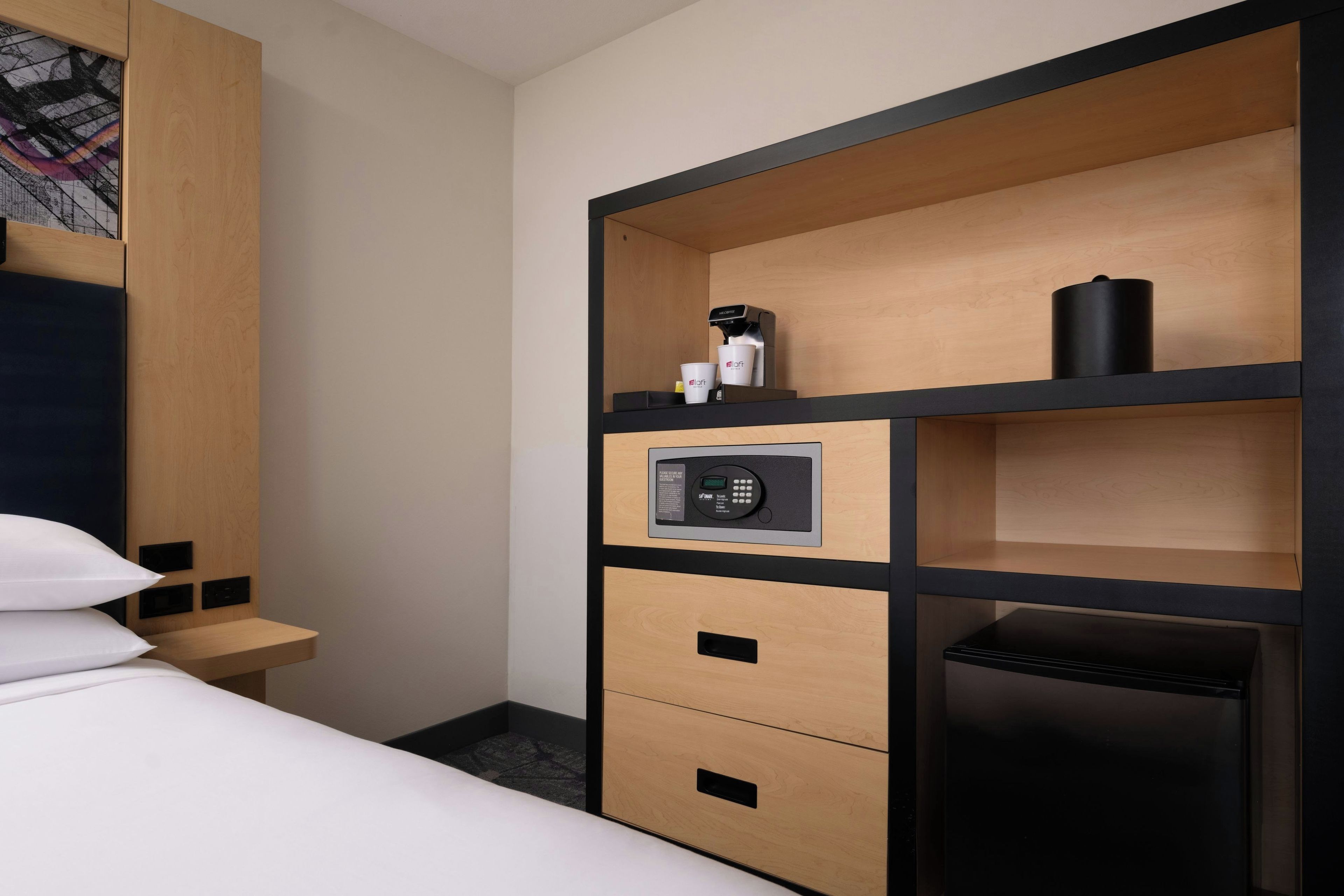 Une chambre d’hôtel équipée d’un lit, d’un minibar, d’une machine à café et d’un panneau de commande.