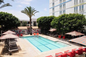 A swimming pool with lounge chairs and umbrellas, surrounded by trees and a building with balconies. - Aloft by Marriott El Segundo - Los Angeles Airport (El Segundo)