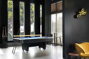 Una mesa de billar con tacos y bolas, una silla amarilla y un letrero de neón en la pared.