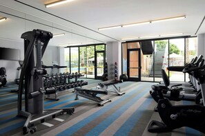 A modern gym with cardio machines, weight stations, and a large mirror. - Aloft by Marriott El Segundo - Los Angeles Airport (El Segundo)