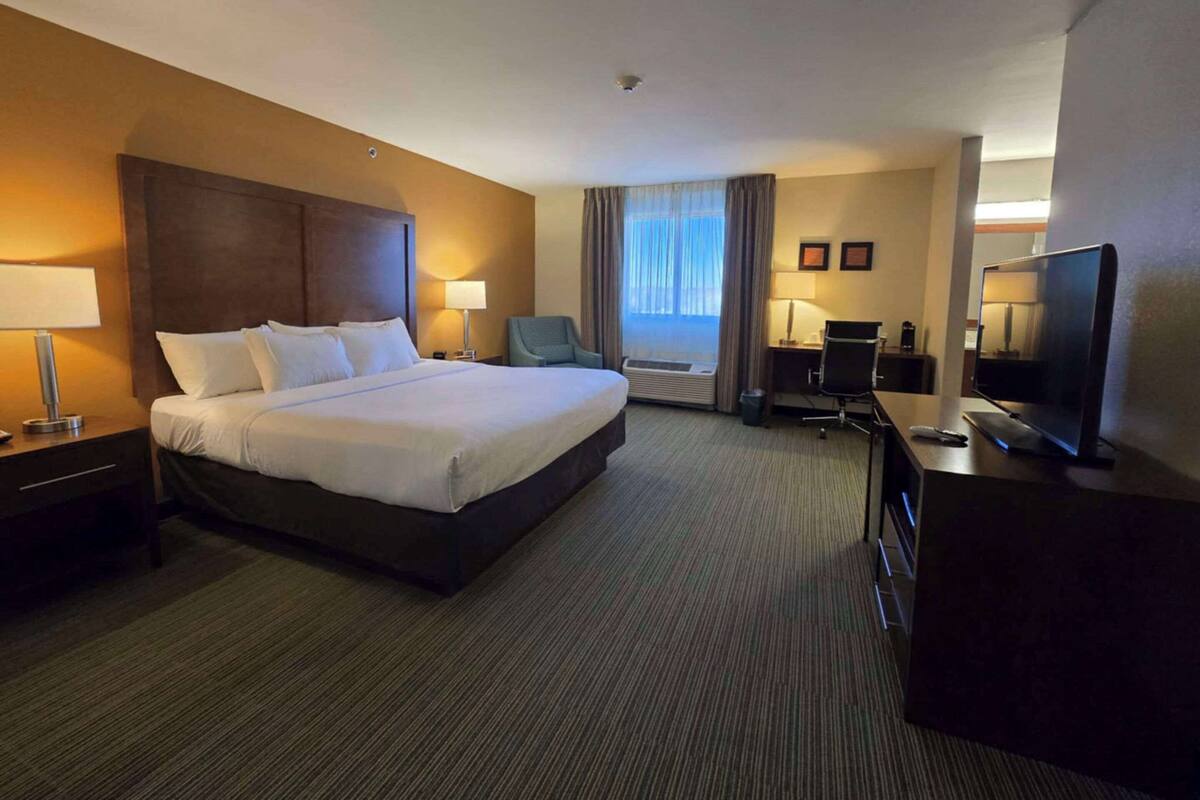 A hotel room with a large bed, a desk with a computer, a TV, and a chair.