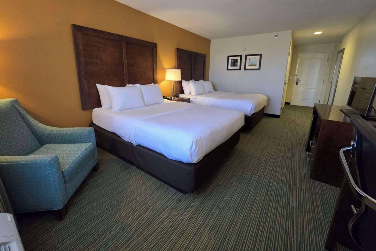 A hotel room with two beds, a sofa, a desk, and a television.