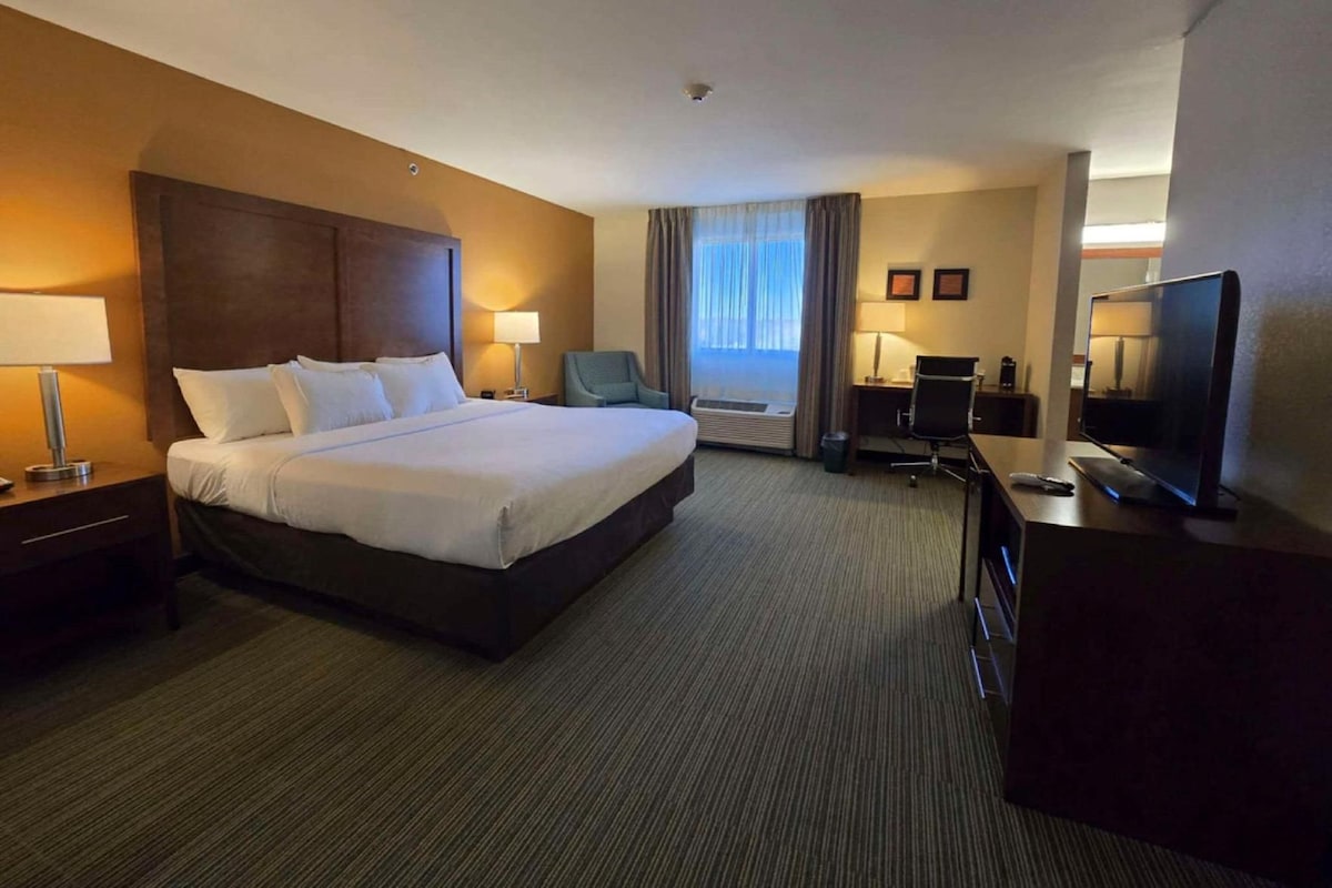 Una habitación de hotel con una cama grande, mesitas de noche, un escritorio con silla, un televisor y una ventana con cortinas.