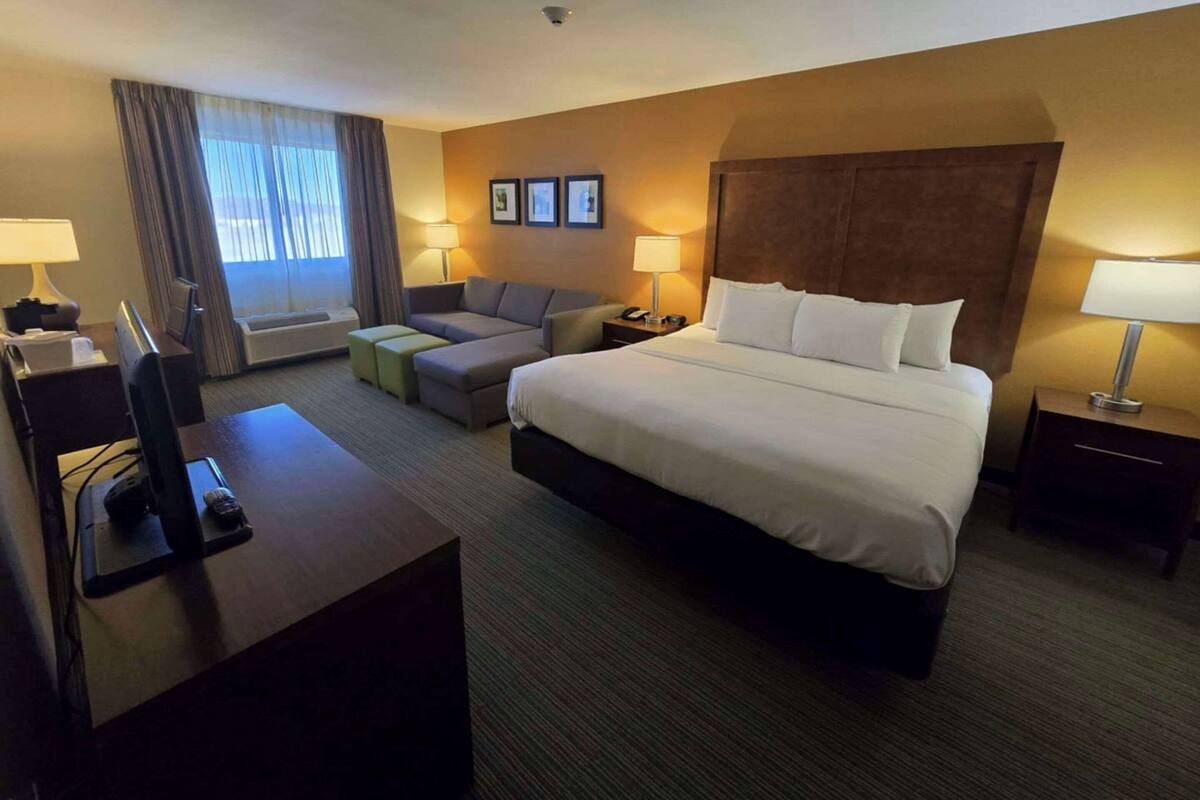 A hotel room with a large bed, a desk with a computer, a sofa, and a TV.