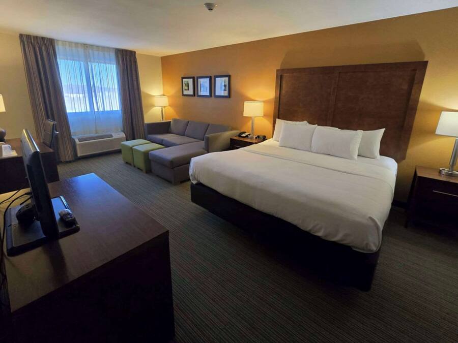 Quarto de hotel com uma cama grande, uma escrivaninha com computador, um sofá e uma televisão.
