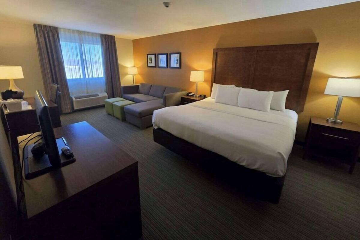 A hotel room with a large bed, a desk with a computer, a sofa, and a TV.
