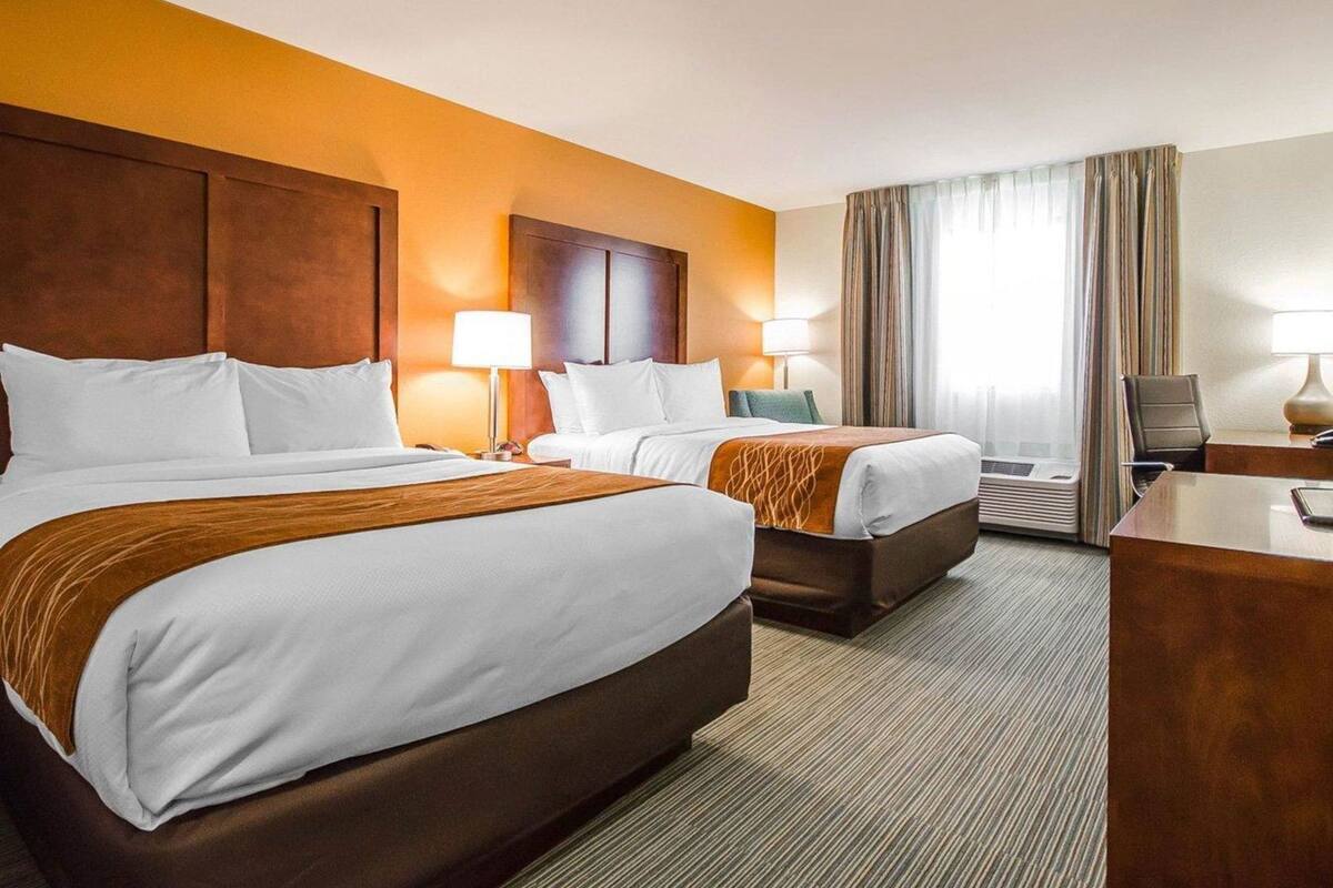 A hotel room with two beds, a desk, a chair, and a television.