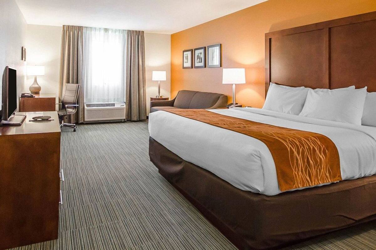 A hotel room with a bed, desk, chair, and a window with curtains.