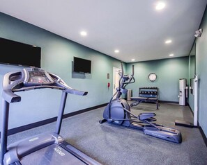 A fitness room with treadmills and elliptical machines, a clock, and a TV on the wall.