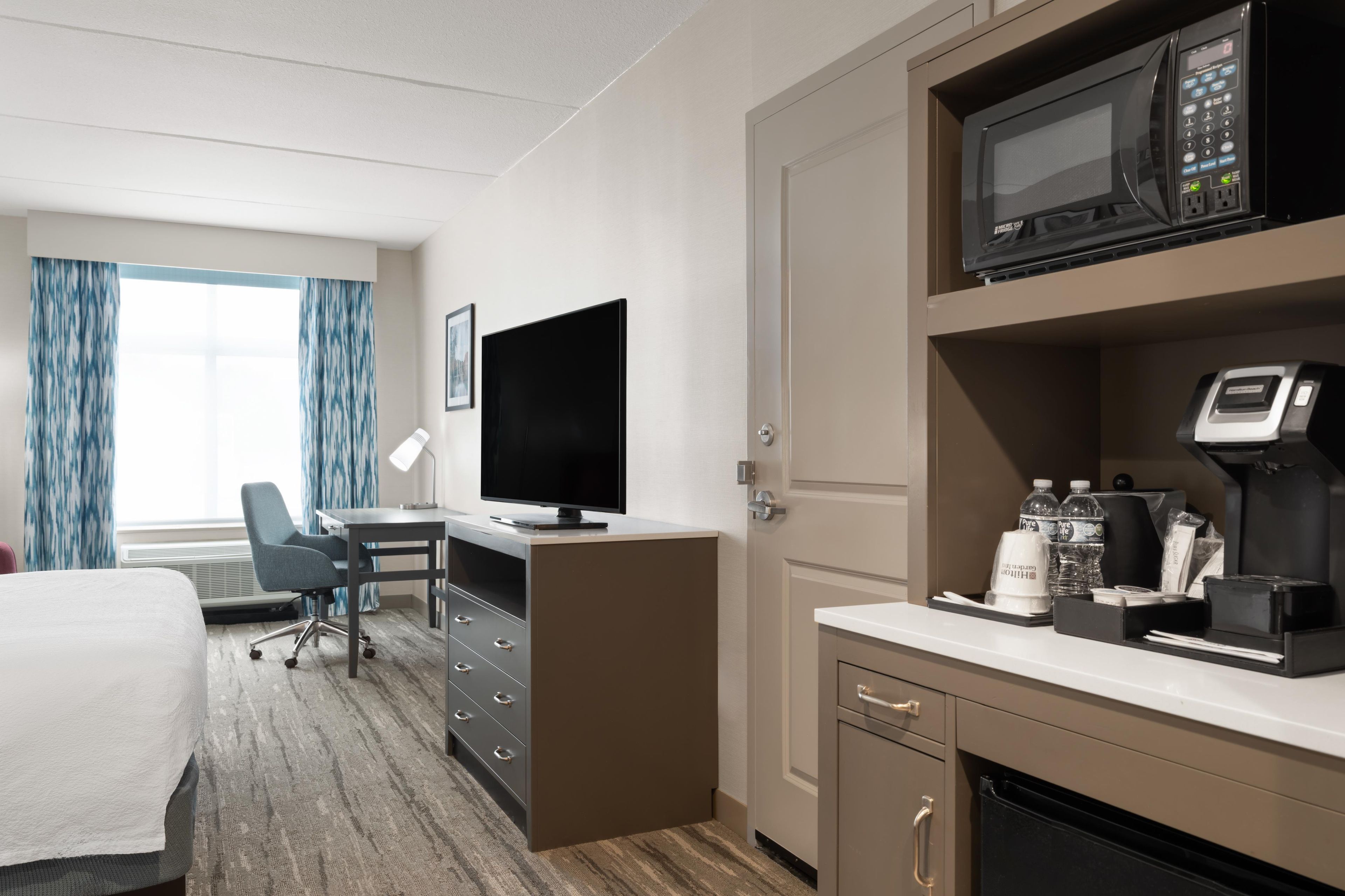Une chambre d’hôtel équipée d’un lit, d’un bureau, d’une télévision, d’un four à micro-ondes, d’une machine à café et d’un mini-bar.