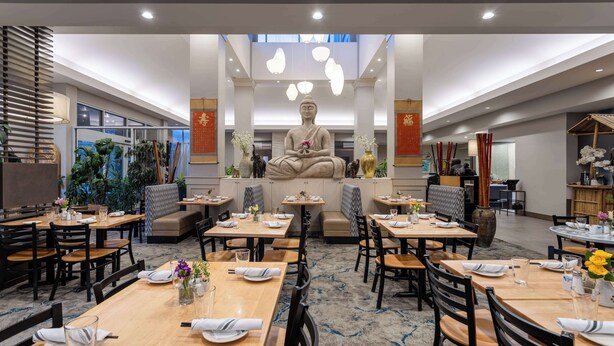 Un restaurant doté d’une grande statue de Bouddha au centre, de nombreuses tables et chaises, et d’un sol recouvert de moquette.
