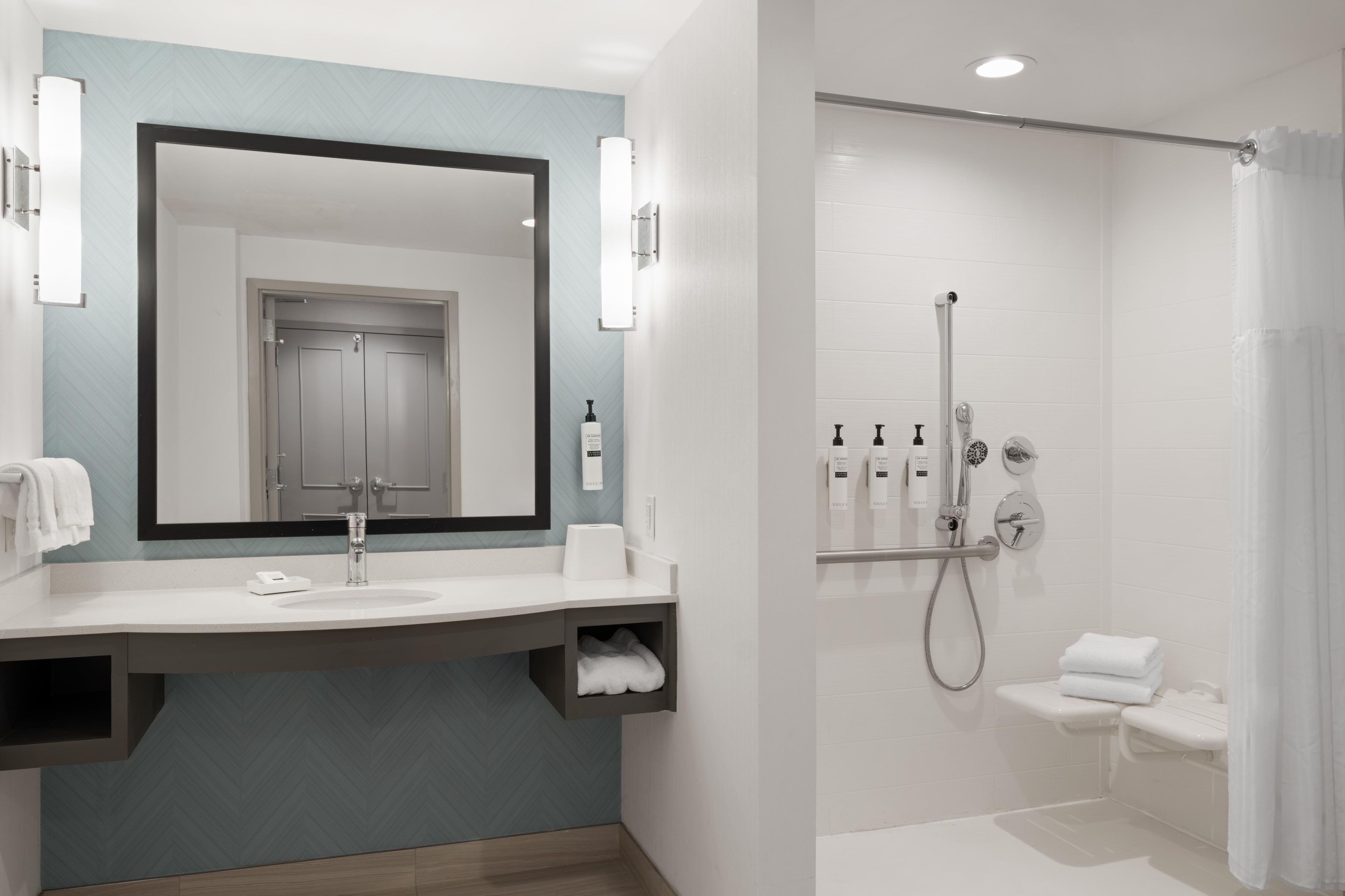 A modern bathroom with a large mirror, a sink, a shower with a handheld showerhead, and a towel rack.