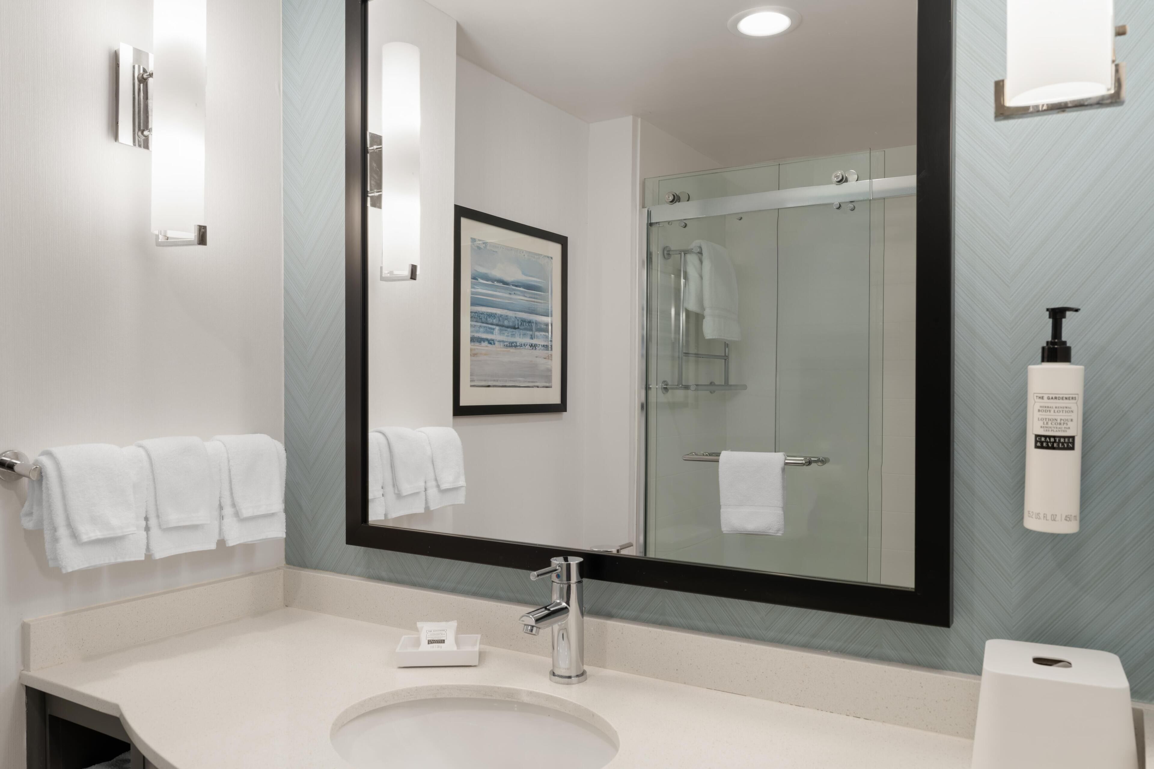 A modern bathroom with a large mirror, a sink, and a shower.
