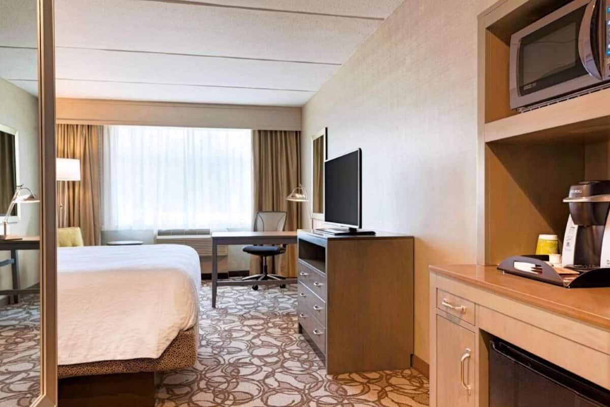 A hotel room with a bed, desk, chair, television, and a microwave.