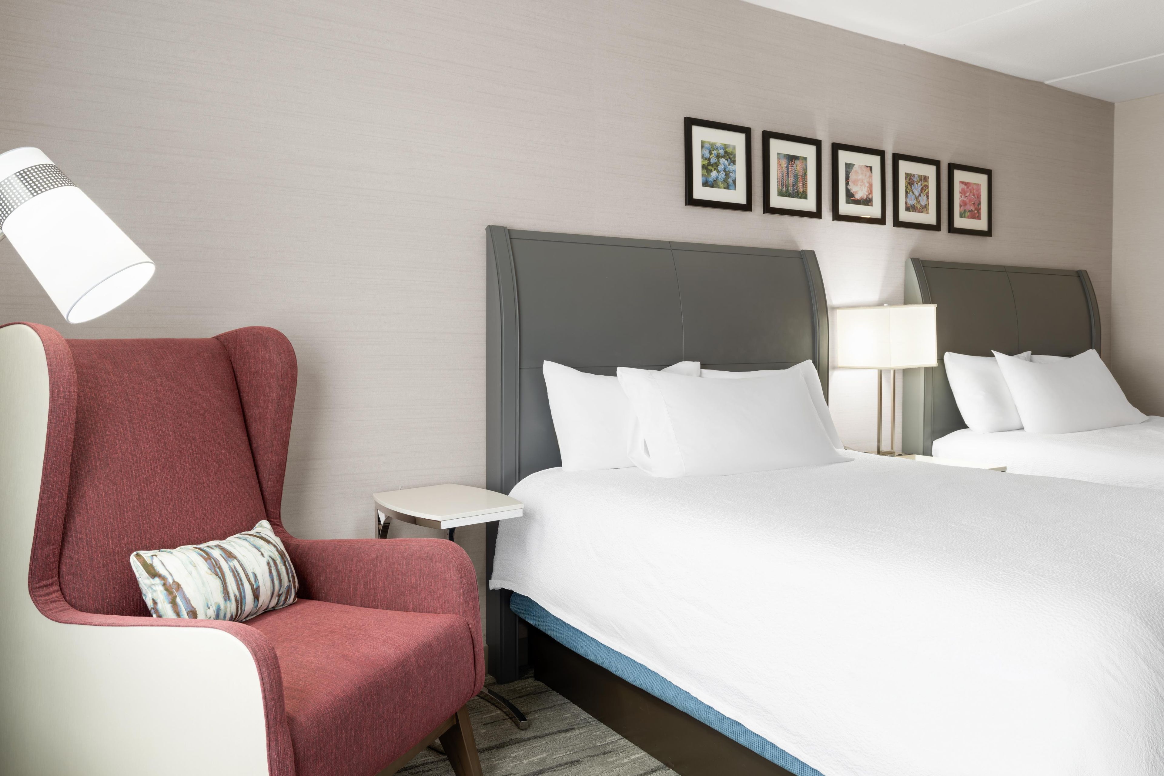 A hotel room with a large bed, a red armchair, a small bedside table, and a nightstand. There are four framed pictures on the wall above the bed.