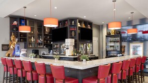 Un espace bar doté d’un îlot central, de tabourets de bar rouges et d’étagères remplies de bouteilles et de verres.