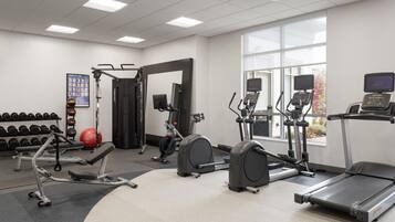 Un gimnasio con máquinas de cardio, mancuernas y una banca.