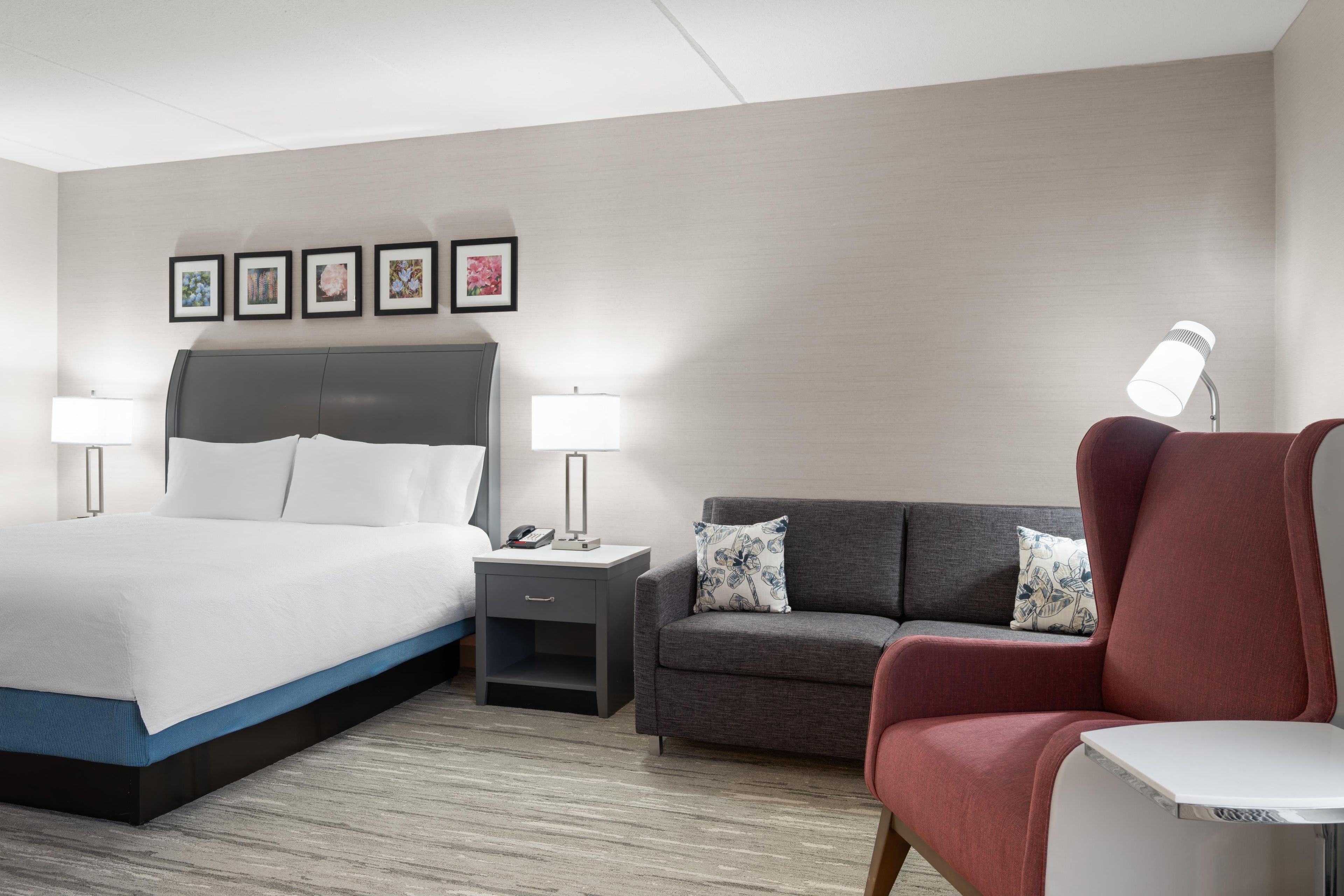 A hotel room with a bed, a nightstand, a desk, a chair, and a sofa.