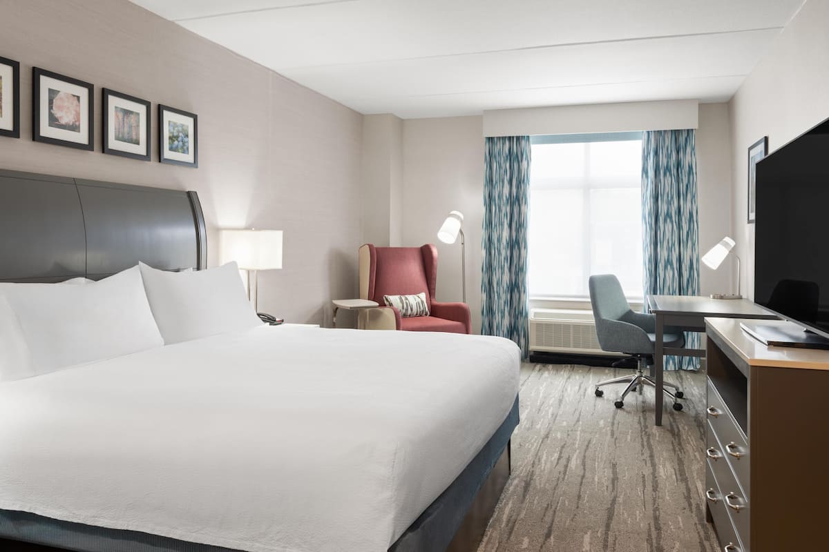A hotel room with a large bed, a desk with a computer, a chair, a lamp, and a TV.