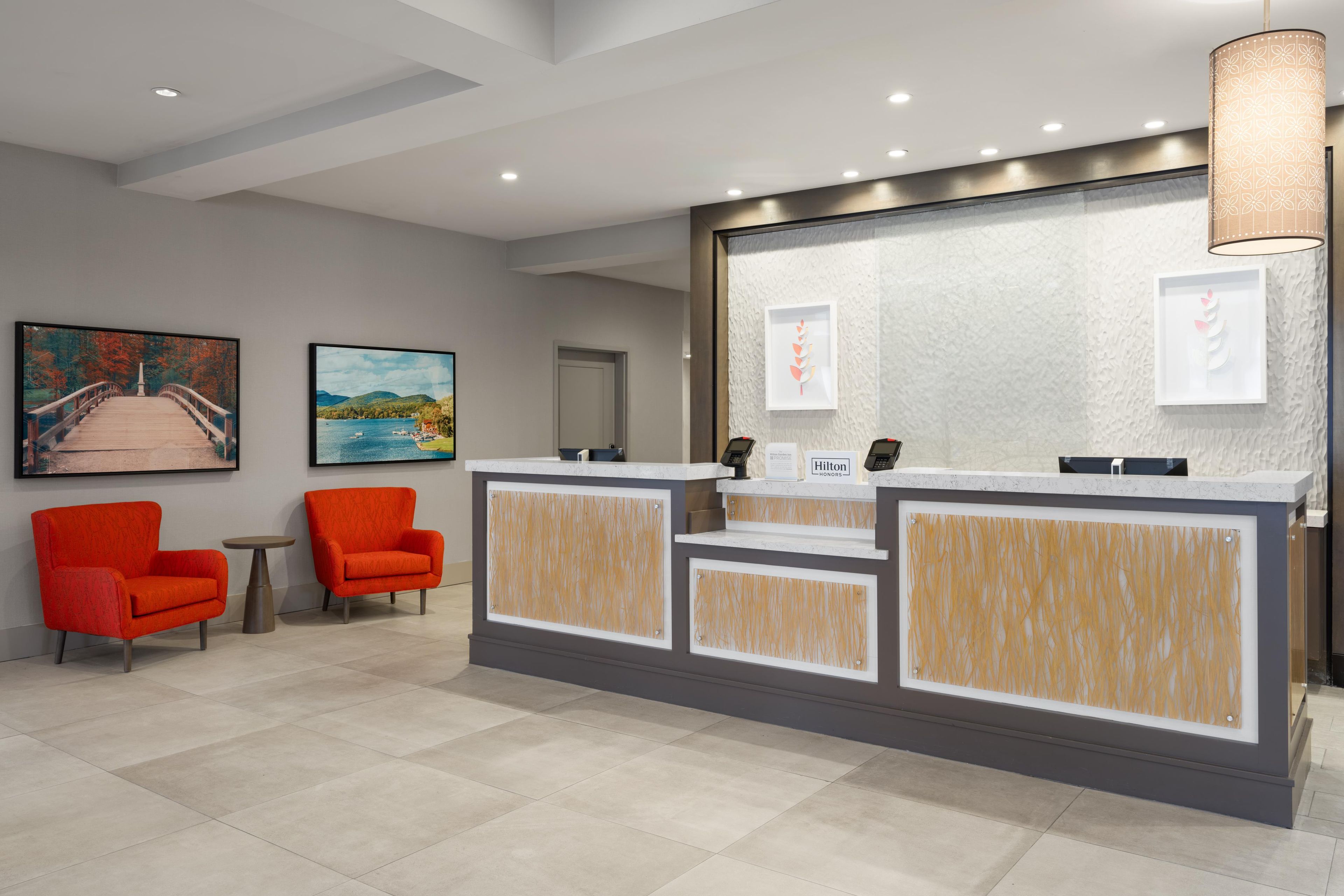 A hotel reception area with a reception desk, two armchairs, a small table, and artwork on the walls.