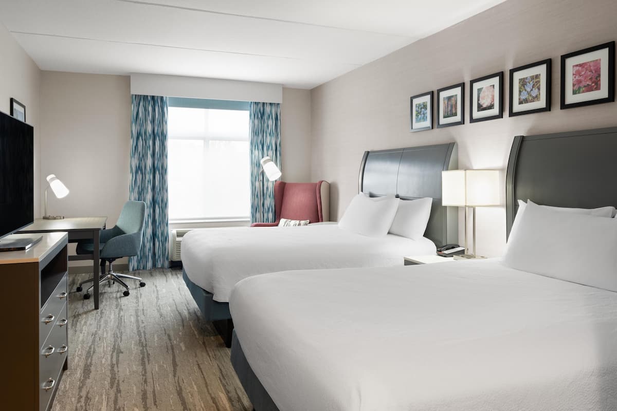 A hotel room with two beds, a desk, a chair, and a TV.