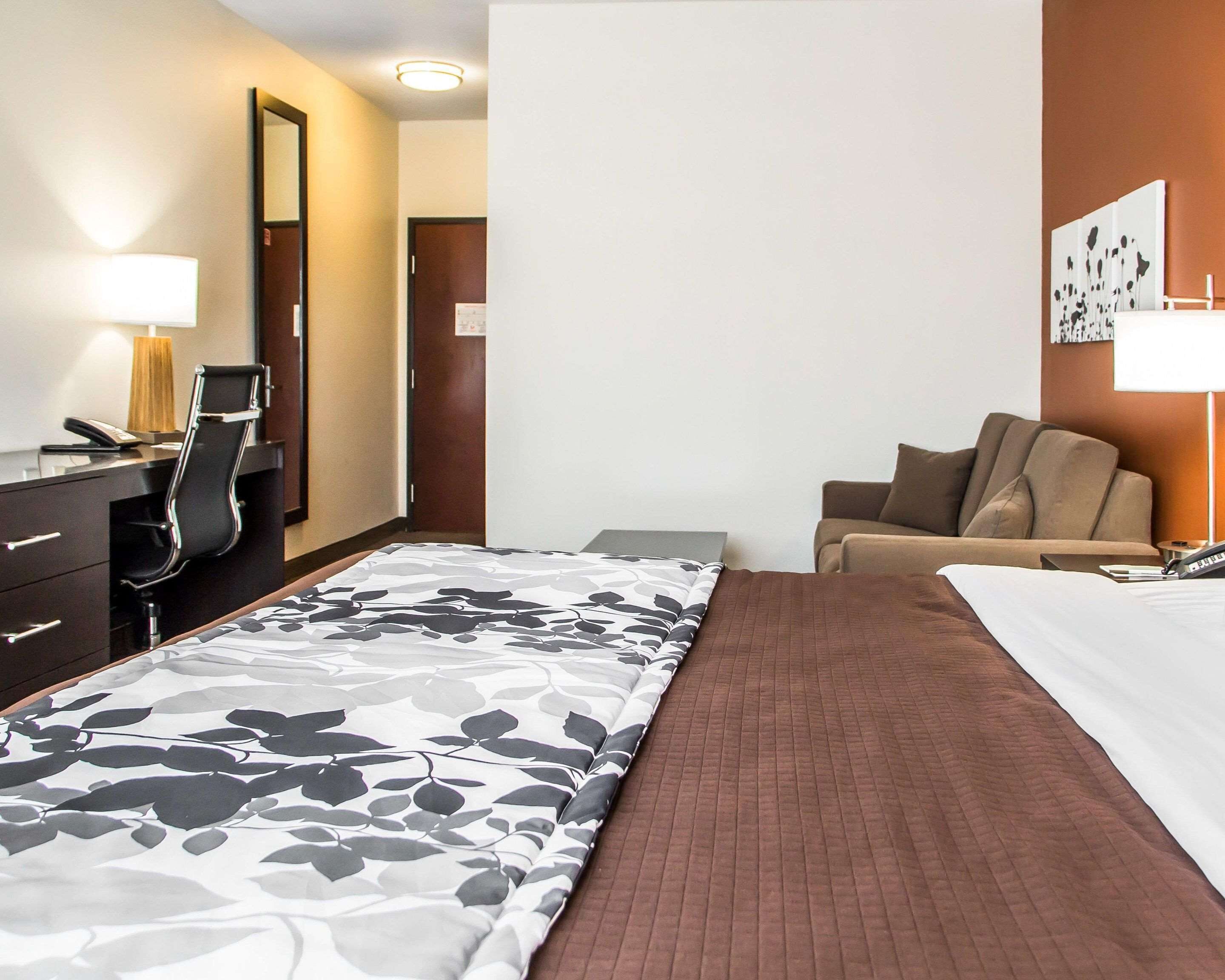 Habitación de hotel con cama, escritorio con silla, lámpara de escritorio, teléfono y una obra de arte colgada en la pared.