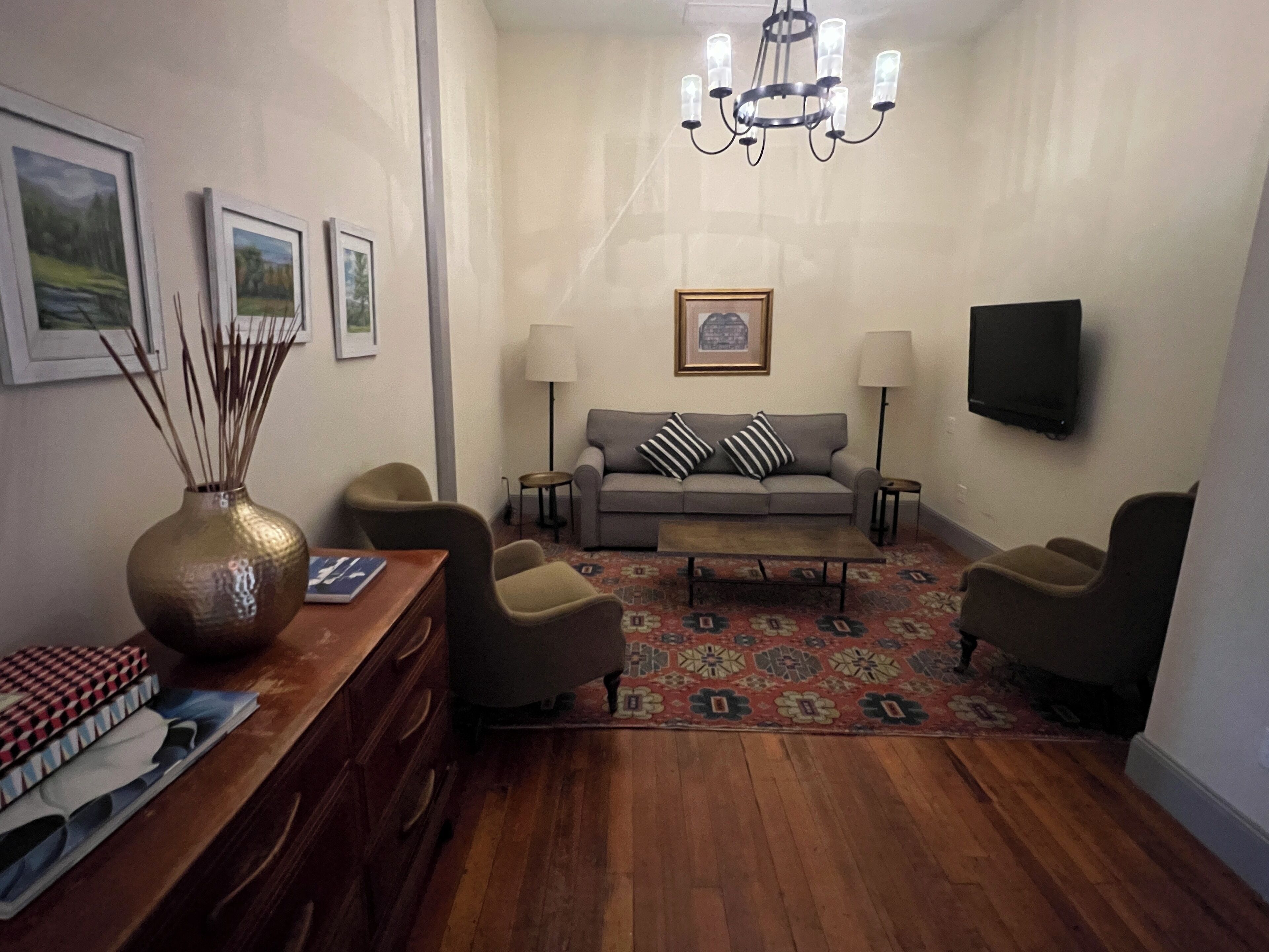 A living room with a sofa, armchairs, a coffee table, a TV, and a chandelier.