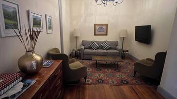 A living room with a sofa, armchairs, a coffee table, a TV, and a chandelier.