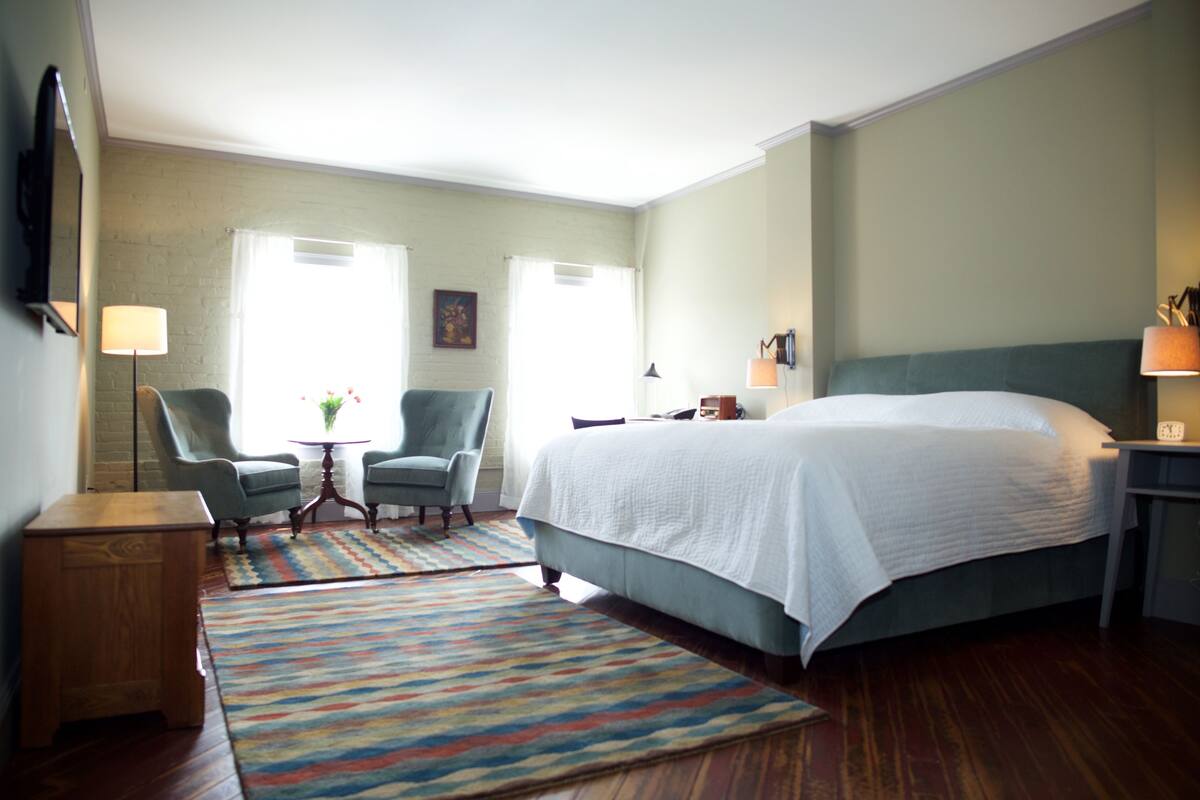 A hotel room with a bed, two chairs, a small table, and a rug.