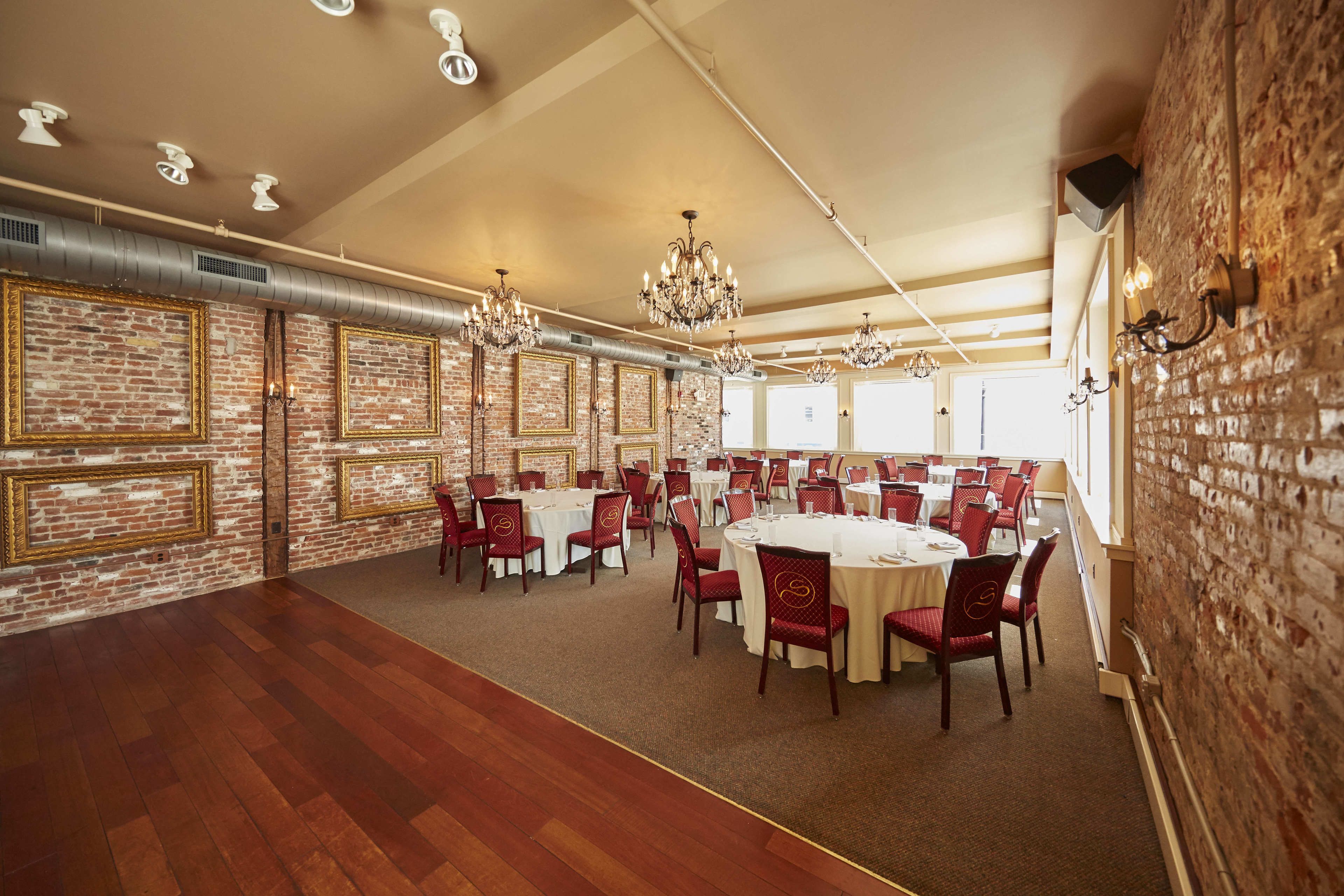 Un amplio salón de banquetes con mesas redondas y sillas rojas, paredes de ladrillo y candelabros.
