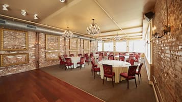 Un amplio salón de banquetes con mesas redondas y sillas rojas, paredes de ladrillo y candelabros.