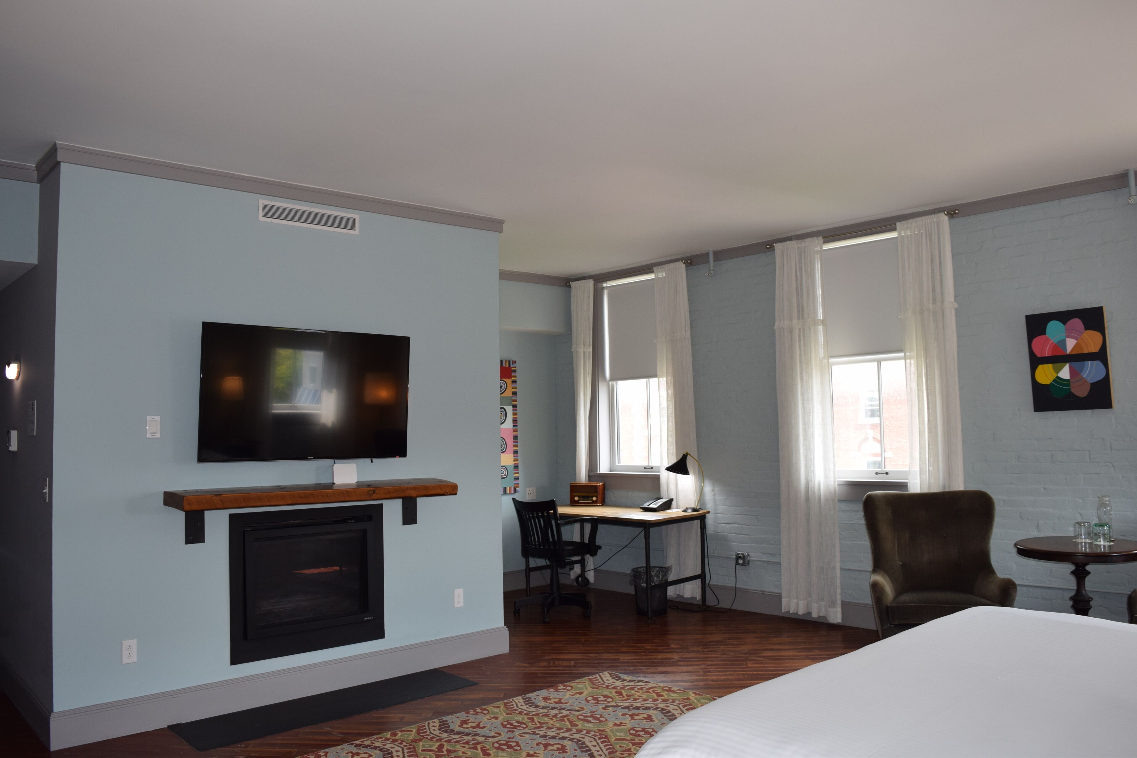 A hotel room with a television, fireplace, desk, chair, and a bed.