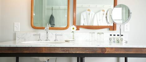 A bathroom with a marble sink, wooden vanity, two mirrors, and toiletries.