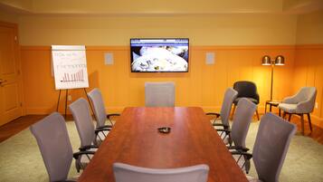 A conference room with a wooden table, six chairs, a whiteboard with a graph, a television on the wall, and a lamp.