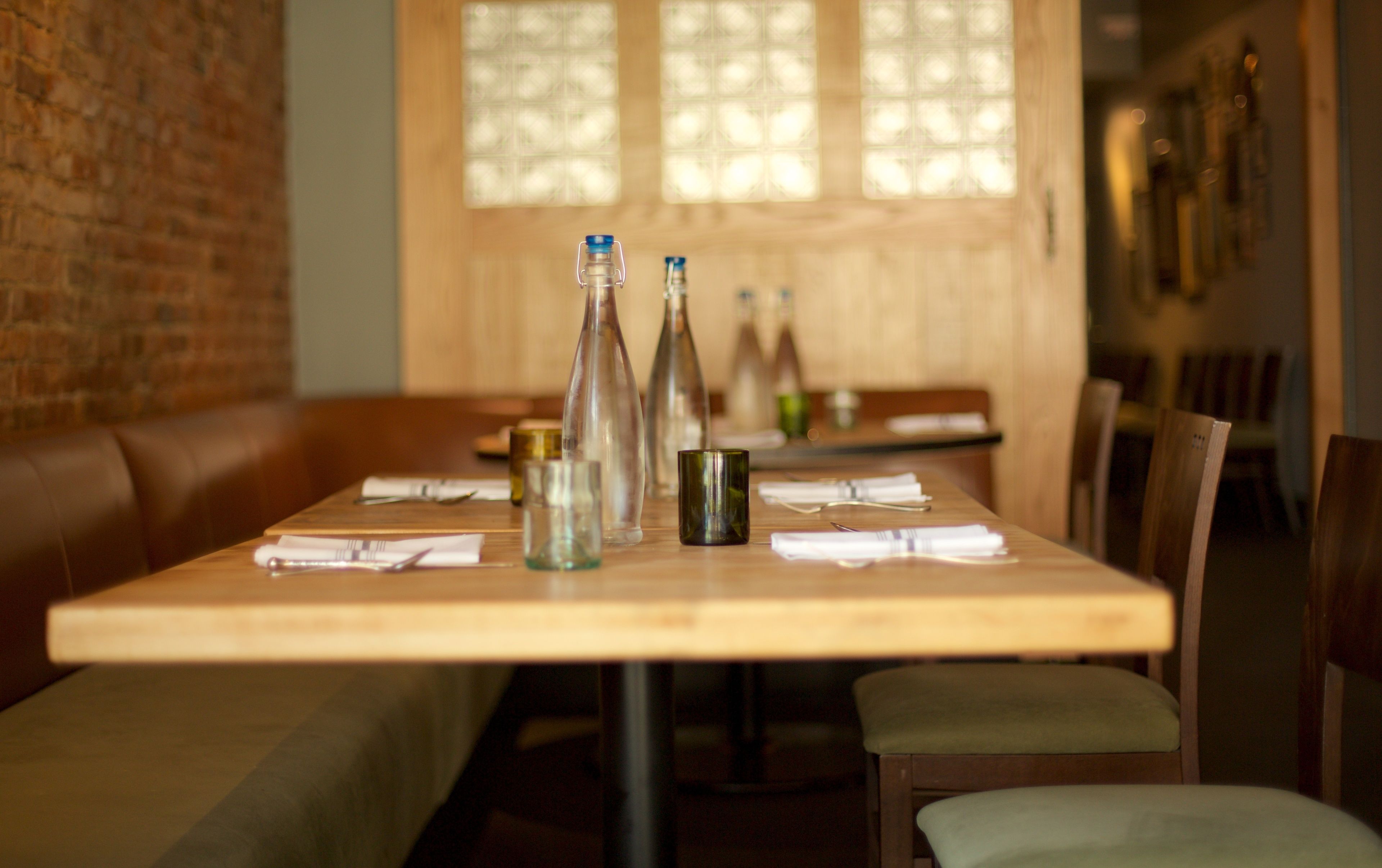Un restaurante con una mesa de madera dispuesta para comer, una pared de ladrillo y una ventana con luz natural.