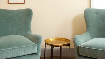 A room with two teal armchairs, a small round table, and three framed artworks on the wall.
